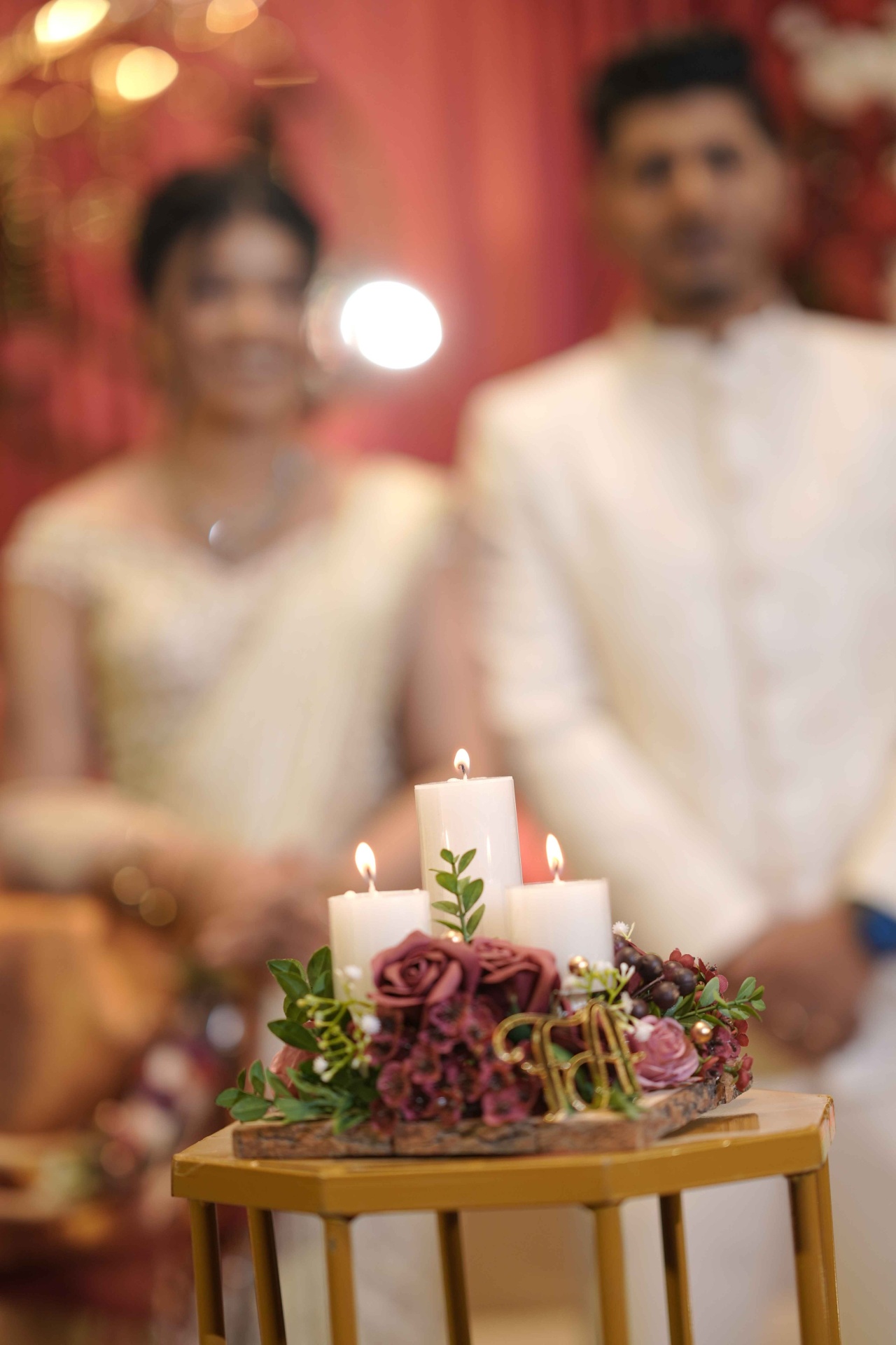Candlelit centerpiece with burgundy florals and couple in background