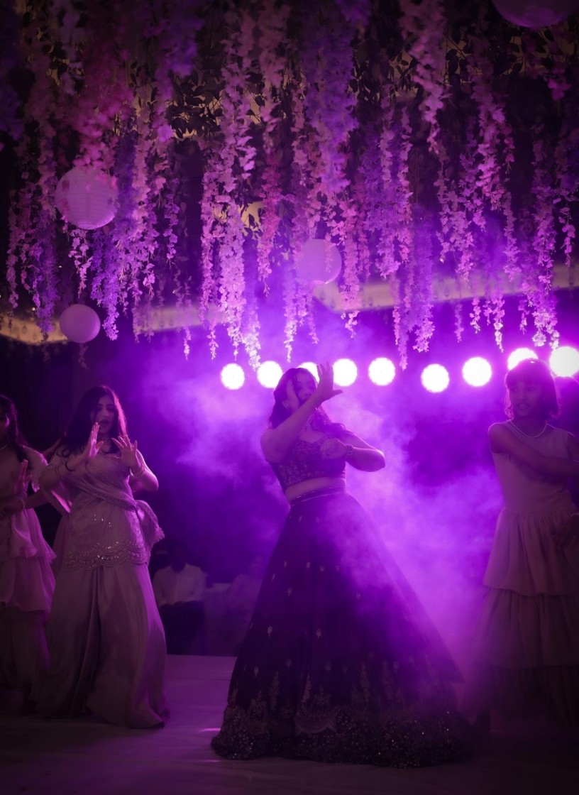 Sangeet performance under wisteria florals and violet stage lights